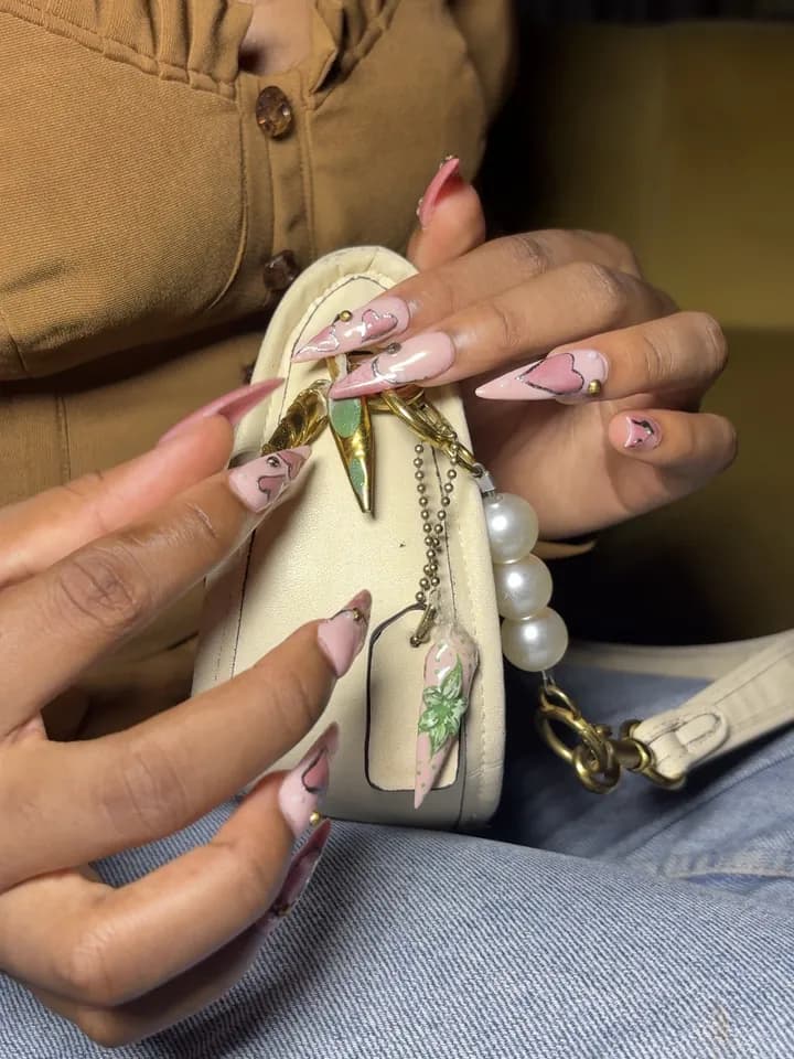 Hands with long pink nails holding a cream bag with a nail charm clipped on