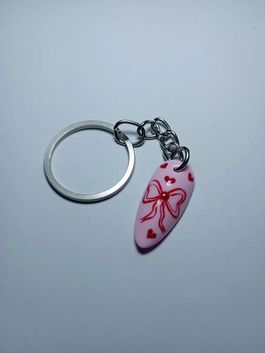 A pink almond nail charm with a hand-painted red bow, on a silver key ring
