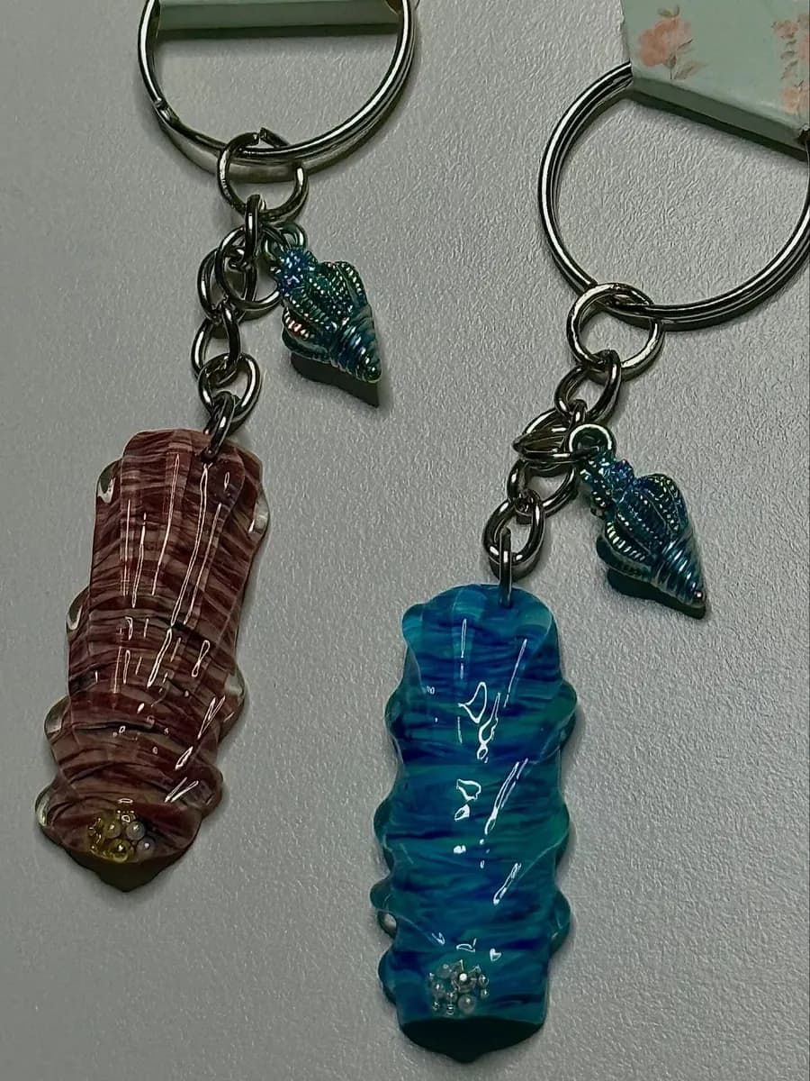Two sculpted nail charms in burgundy and ocean blue, each with a shell charm, on key rings